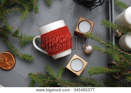 White And Red Ceramic Mug On Gray Textile With Candles And Spruce Branches