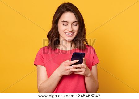 Horizontalshot Of Smiling Woman Holding Mobile Phone And Text Messaging, Looking At Her Device's Scr