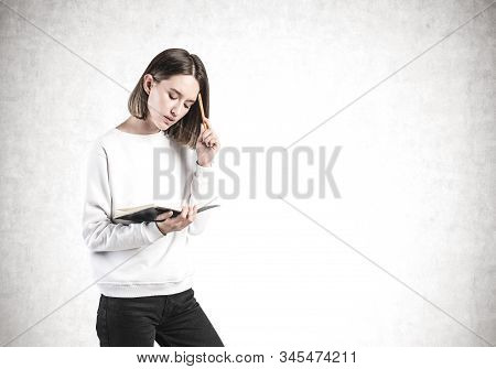 Portrait Of Thoughtful Young Girl In Casual Clothes With Notebook And Pen Standing Near Cocnrete Wal