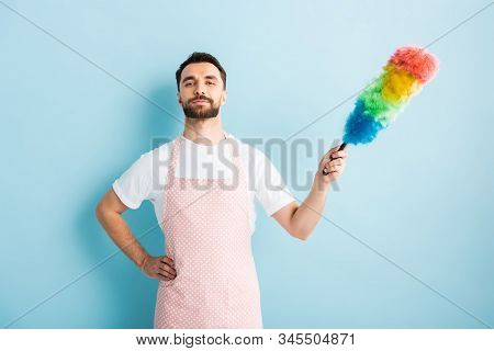 Handsome Man In Apron Holding Dust Brush On Blue