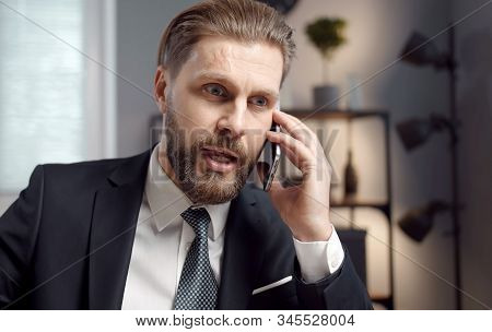 Portrait Of Vigorous Bearded Adult Businessman In Formal Suit Talking On Phone In Office