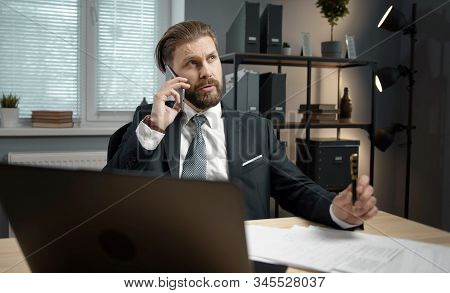 Thoughtful Bearded Mature Businessman Wearing Classic Suit Talking On Mobile Phone Sitting At Table 