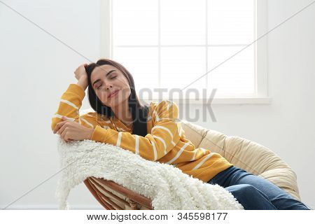Young Woman Relaxing In Papasan Chair Near Window At Home
