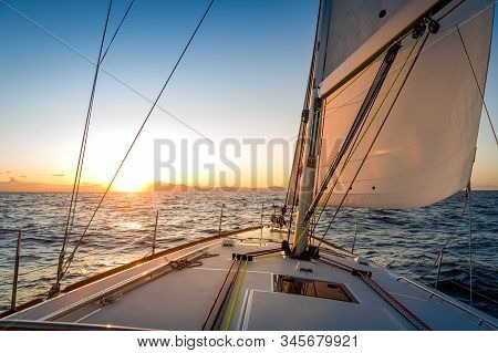 Chasing The Sun At Sailing Yacht. Deck And Sails Of Sailoat Pointing To The Sunrise. Mediterranean S