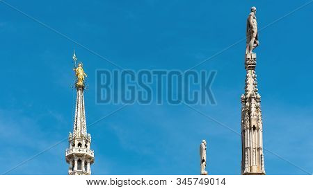 Milan Cathedral Spires, Italy. Golden Statue Of Madonna And Other Sculptures On Blue Sky Background.