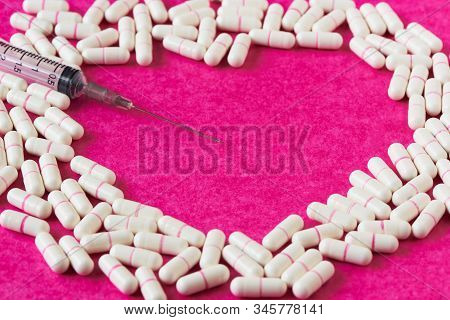 A Plastic Syringe With Needle On The Capsule Of Drugs Arranging In Heartt Shaped Space