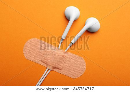 Wired Earphones With Sticking Plaster On Orange Background, Flat Lay