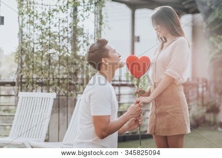 Romantic Happy Asian Man On His Knee Give Heart Shape Flower To His Girlfriend. Vanlentine Day Conce
