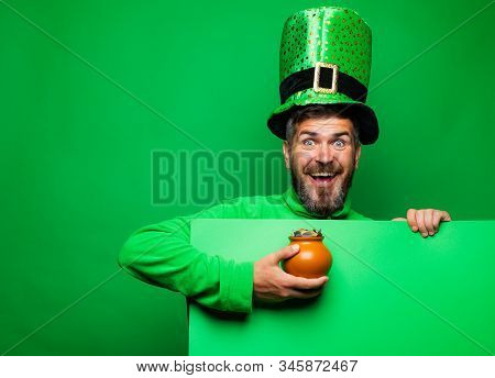 Bearded Man Celebrating Saint Patricks Day. Leprechaun Man In Green Hat And Hoodie Holding Pot Of Go