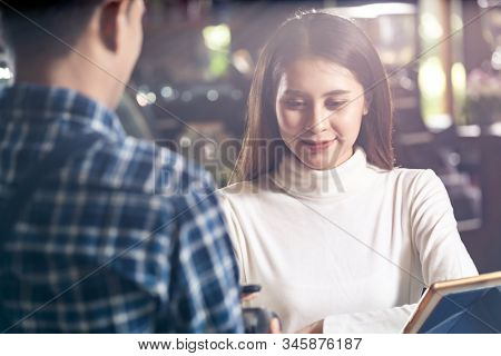 Asian woman customer using mobile phone scane QR code on credit card reader EDC machine to pay a waiter for coffee purchase at table in cafe.