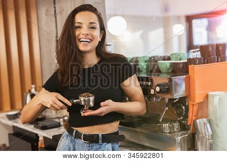 Smiling Barista Woman Standing Behind The Bar With Coffee Holder Full Of Coffee Beans In Her Hands ,