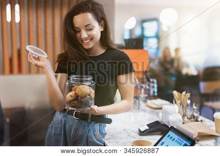 Young Smiling Beautiful Woman Barista Standing Behind The Bar, Enjoys Nice Aroma While Opening Jar W