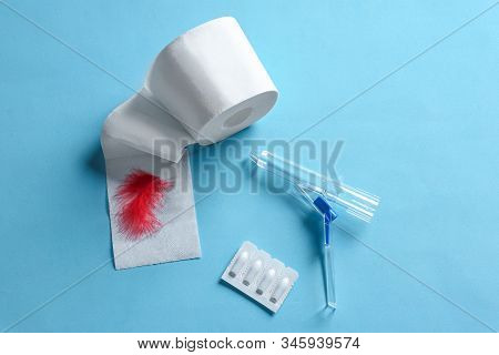 Anoscope, Suppositories And Toilet Paper With Red Feather On Light Blue Background, Flat Lay. Hemorr