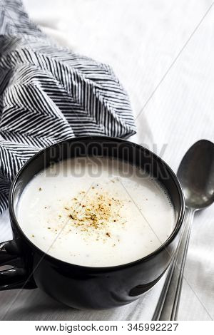 Cauliflower Soup (creme Du Barry) In Black Bowl On White Background With Black And White Cloth.