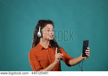 Young Woman With Headphones Talking During A Conference Over Smart Phone Against Green Background.