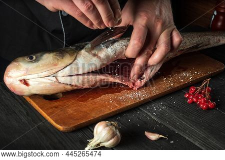 The Chef Prepares Silver Carp Herring In The Restaurant Kitchen. The Cook Sprinkles Salt On The Fish