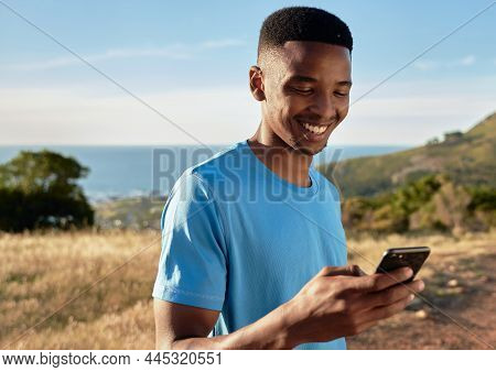 Black Young Adult Male Smiling While Using His Cellphone, About To Start Mountain Walk. Beautiful Ou