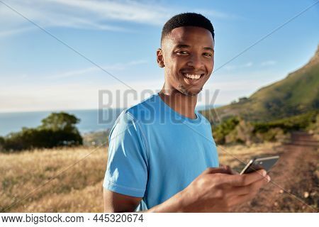 Portrait Of Black Young Adult Male Smiling At The Camera While Using His Outdoors On Mountain About 