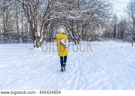 Young Woman In Yellow Jacket With Ice Skates Walking Through Snowy Park