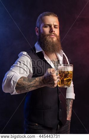 Portrait Of Bearded Man Who Holds Mug Of Beer In His Tattoos Hand Looking At Camera Over Black Backg