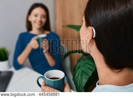 Adult Woman With A Hearing Impairment Uses A Hearing Aid To Communicate With Her Female Friend Durin