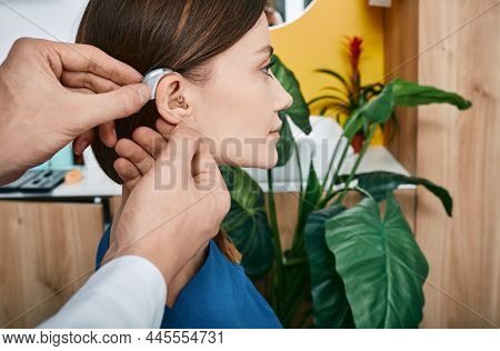 Hearing Treatment For Hearing Impaired People. Caucasian Woman During Installation Hearing Aid Into 