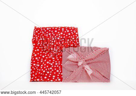 Two Gifts Wrapped In Red Holiday Furoshiki Wrapping Cloth With Stars, Candy Cane Tripes And Shepherd