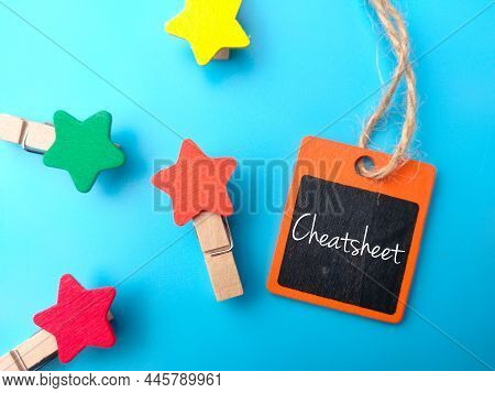 Colored Wooden Tag And Wooden Clips With Text Cheatsheet On Blue Background.