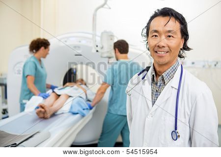 Portrait of mature radiologist with nurses preparing patient for CT scan in hospital