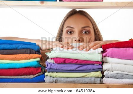 young woman hiding behind a shelf with clothing, isolated on white background