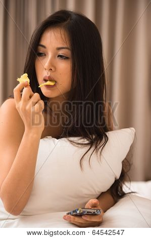 Asian Young Woman Eating Potato On The Bed In The Hotel Room