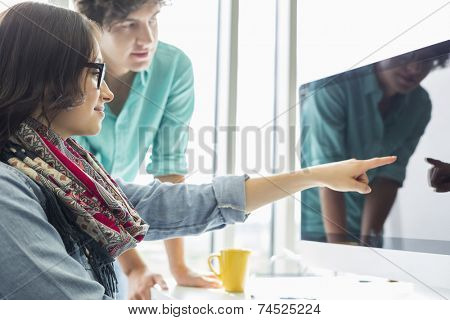 Creative businesswoman showing something to colleague on desktop computer in office
