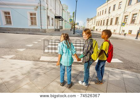 Three kids holding hands stand on street