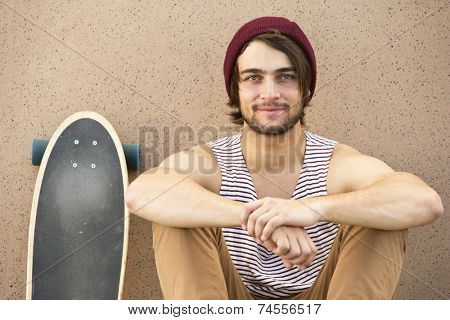 Young skateboarder, sitting against a granite wall, looking defiantly into the camera, with a confident smirk on his face