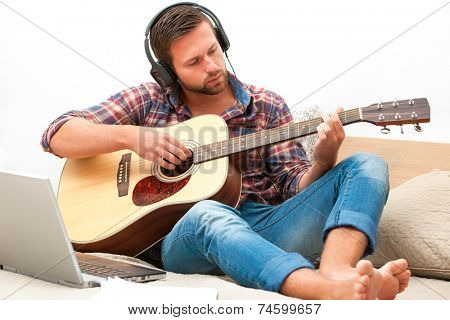 Man on sofa playing the guitar with laptop at home