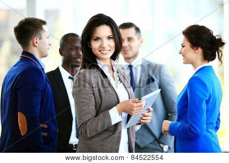 Business woman standing in foreground with a tablet in her hands, her co-workers discussing business