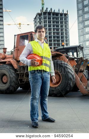 Foreman In Yellow  Jacket Posing Next To Bulldozer On Building Site