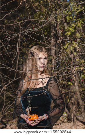 Portrait Of A Young Long-haired Blond Girl In A Black Dress Posing With A Pumpkin