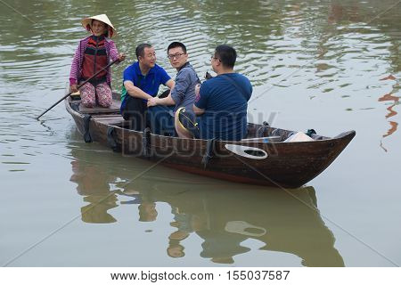HOI AN, VIETNAM - JANUARY 02, 2016: The boatwoman rides the chinese tourists on the old national vietnamese boat down the Thu Bong river. The tourist landmark