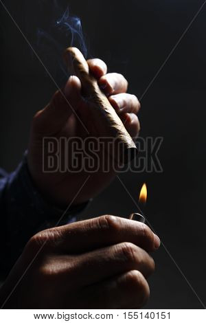 Cigar with smoke in one hand and lighter in another hand