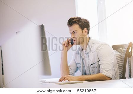 serious man talking on mobile phone while using laptop computer at desk in study. Looking of the working men in the office. The guy makes a business call