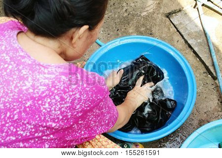 Hands washing clothes in a basin at ourside