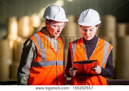 Paper mill factory workers with giant paper rolls on the background