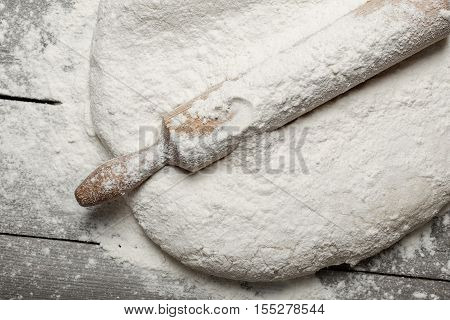 Rolling pin with flour close up on wooden table in bakery top view. Bakery background