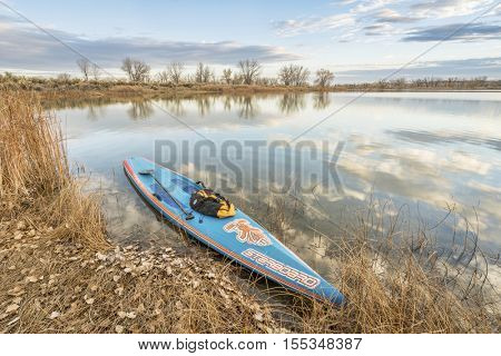 FORT COLLINS  CO, USA - November 5, 2016: All Star racing stand up paddleboard by Starboard in brushed carbon layout with Werner paddle and duffel on a shore of a calm lake with late fall scenery