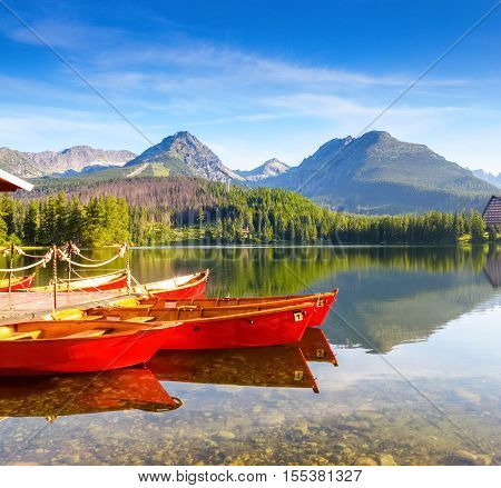 Dreamy red boats stand at the pier on a quiet lake with a beautiful view of the mountains.Strbske Pleso lake Slovakia Tatra mountains