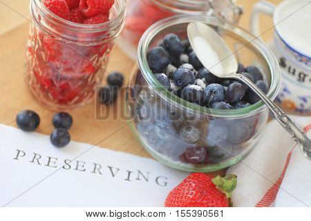 Blueberries raspberries and strawberries in glass jars with sugar ready for making jam