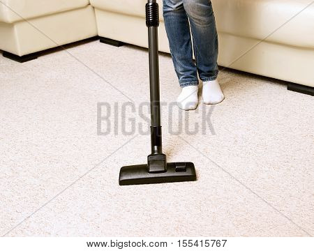 girl in jeans vacuuming the house. bright carpet and light leather sofa