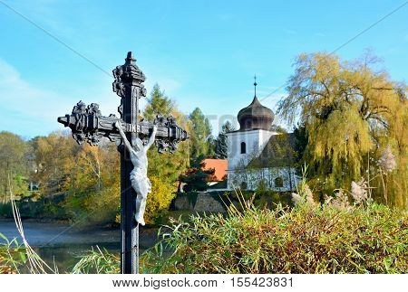 Jesus on cross outside in nature with church in background.