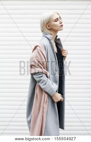 Stylish blonde girl in grey coat on white background